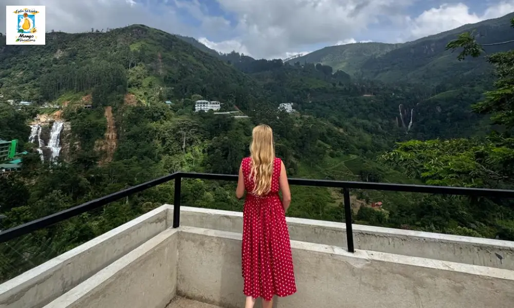 A traveler in a red dress stands on a scenic viewpoint overlooking the lush mountains of Nuwara Eliya, Sri Lanka, with cascading waterfalls and misty green valleys stretching into the distance.